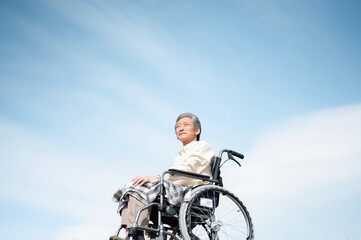 Obraz premium 青空をバックに車椅子に乗るシニア男性