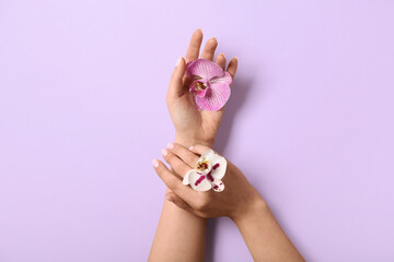 Woman with orchid flowers on lilac background. Hand care concept