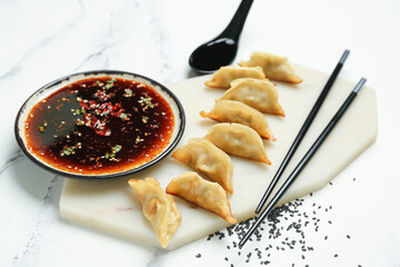 Tasty Chinese jiaozi, sauce and sesame on light background