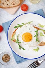 Delicious sandwich with fried egg, avocado and arugula on light background