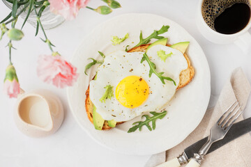 Delicious sandwich with fried egg, avocado and arugula on light background