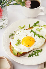 Delicious sandwich with fried egg, avocado and arugula on light background