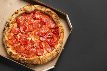 Cardboard box with delicious pepperoni pizza on black background