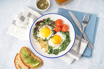 Plate with tasty fried eggs, salad and avocado sandwich on light background
