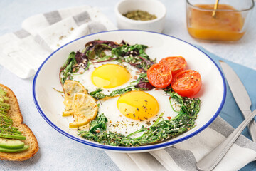 Plate with tasty fried eggs, salad and avocado sandwich on light background