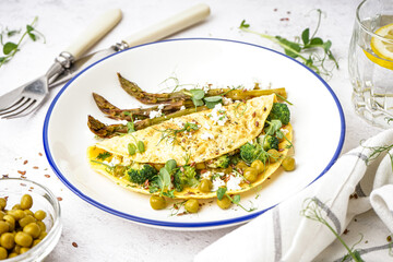 Tasty omelet with broccoli, asparagus and pea on light table