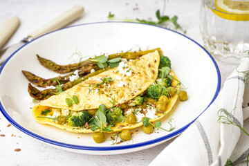 Tasty omelet with broccoli, asparagus and pea on light table