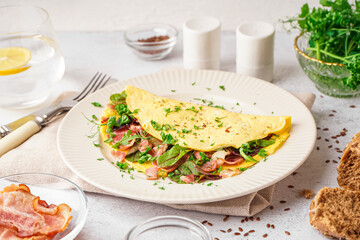 Tasty omelet with ham and greens on light table