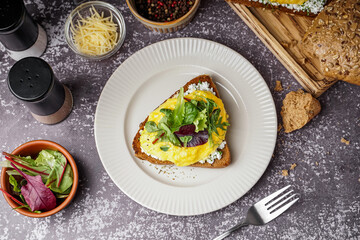 Plate with tasty scrambled eggs sandwich on grey grunge background