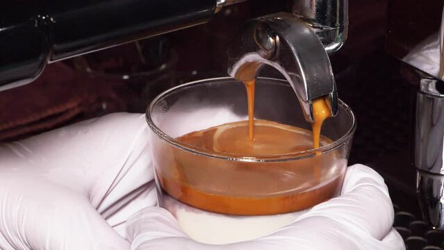Slow motion speed closeup scene on barista hands that rotate cup with frappe in a bottom to get an espresso shot from machine to make dirty coffee style, hygienic coffeehouse, clean cafe.