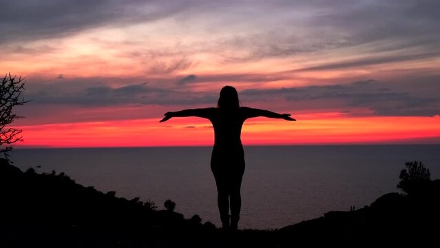 A woman's silhouette gracefully spreads her arms, embracing the stunning crimson sunset