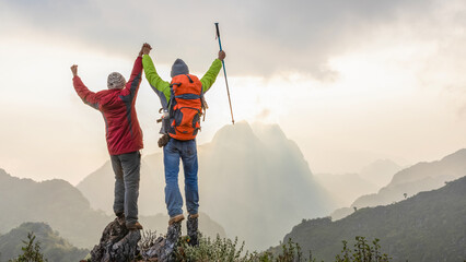 Successful two hiker standing with raised hands relaxing on top mountain landscape enjoy beautiful...