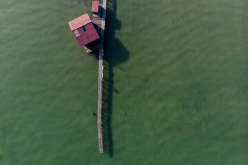Fototapeta na wymiar Aerial top down view of a long wooden dock with a small red colour zinc roof wooden houses on green colour sea as background