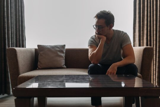 Lonely asian man sits on the sofa thinking of his lover.