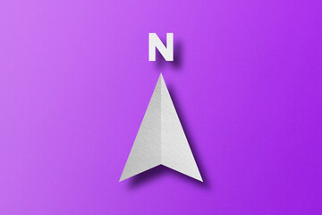 White paper cut in north arrow shape set on purple paper background.