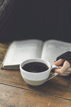 A Womand Hand Holding A Black Coffee With A Reading Book