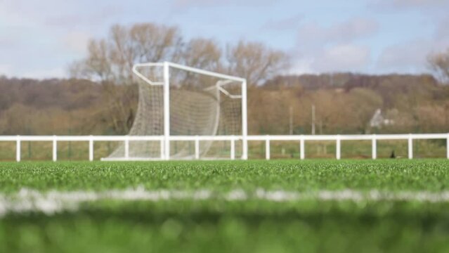 Low shot pulling focus from grass on a football pitch to a football goal net blowing in the wind. Still shot.