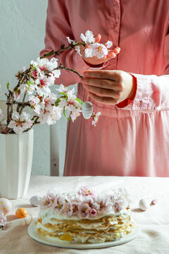 crepe cake or blini cake for Easter party, rose pink background, almond flowers, rose pink background, woman hands