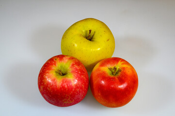 three apples, two red and one yellow of a different variety, class, or type, one pinklady, another royal gala, and the third golden apple, whole on a white cutting board