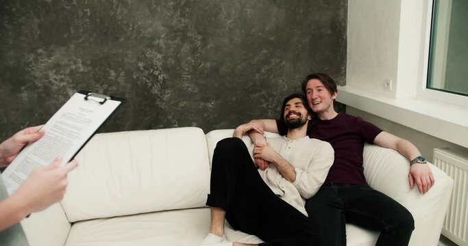 Happy gay couple with real estate agent relaxing on sofa, excited about their new apartment - Powered by Adobe