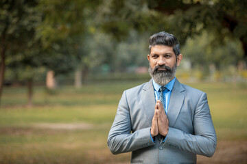 Indian businessman giving namaste or welcome gesture at park.