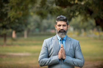 Indian businessman giving namaste or welcome gesture at park.