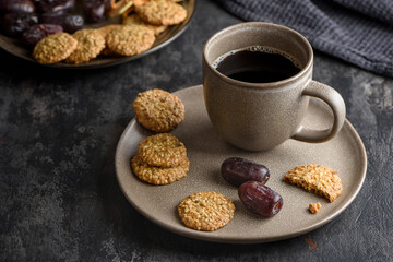 A cup of coffee on a plate with dates and cookies.