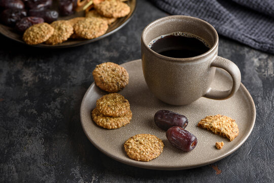 A cup of coffee on a plate with dates and cookies.