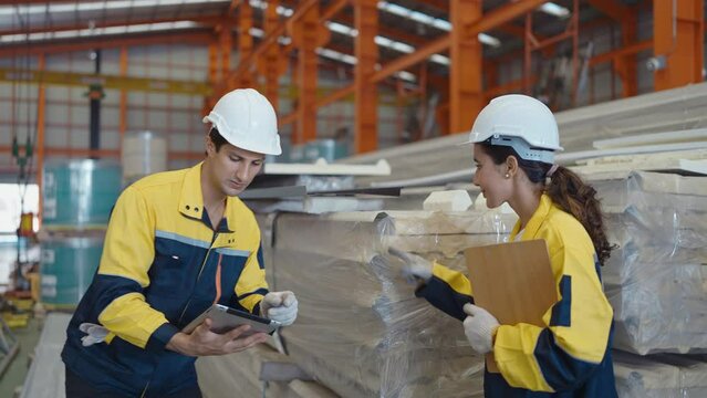 Warehouse worker Hispanic Latin man and woman wearing hard hat and uniform holding tablet checking stock condition in warehouse retail store industry factory. Shipment service