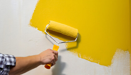 Background texture of a hand applying yellow paint to a wall with a roller, worker painting wall