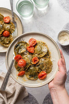 Spinach and broccoli vegan ravioli with cherry tomatoes on a white background