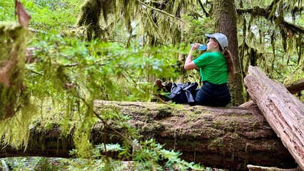 Girl in hike. Traveler in mountain forest Teenage girl in green shirt Sitting on fallen tree She takes bottle of water from her backpack and drinks. MacMillan Provincial Park canada vancouver island 