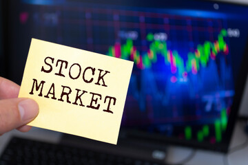 Male hand holding sticky note written STOCK MARKET.