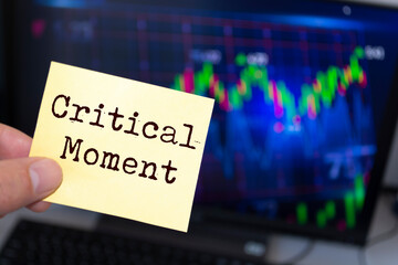 Male hand holding sticky note written Critical Moment.