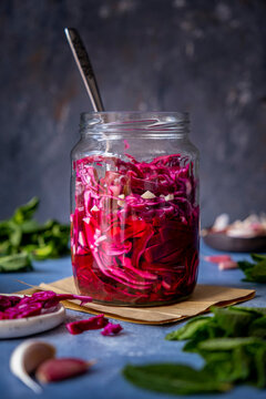 A jar of pickled red cabbage and a fork inside it photographed on a dark backdrop.