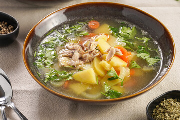 two deep green bowls with traditional european chicken soup with potato, carrots, celery, fresh parsley on a beige colored kitchen table cloth