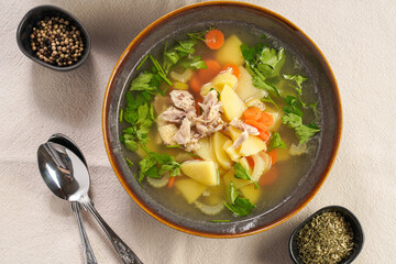 two deep green bowls with traditional european chicken soup with potato, carrots, celery, fresh parsley on a beige colored kitchen table cloth, top view