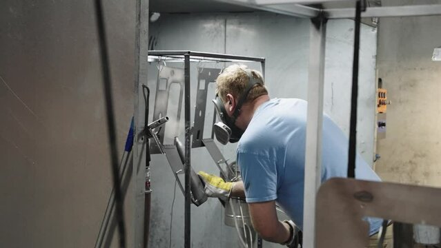 Slow motion, blue collar worker applying powder coating on metal with paint gun in workshop