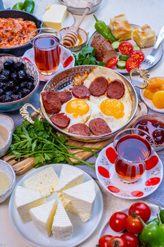 Turkish breakfast table from front view. Eggs and sujuk in a copper pan. Olives, cheese and Turkish tea in tulip glasses around it.