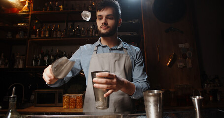 Cool professional caucasian bartender making a cocktail, muddling ice with beverage in his shaker. Authentic barman making alcohol drink using special equipment 