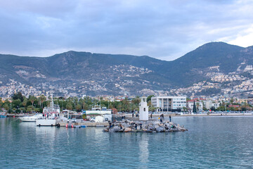 Fototapeta na wymiar Beautiful view on a town, mountains, sea, lighthouse and ships in Alanya port, Turkey