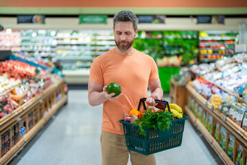 Man with shopping basket full of vegetables and fruits. Middle aged millennial man in a food store....