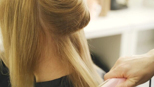 The stylist straightens the hair of a woman client with a hair straightener. Close-up. BRAZILIAN HAIR STRAIGHTENING