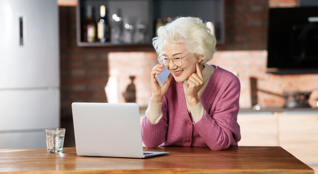 Elegant older woman making phone calls while using a computer
