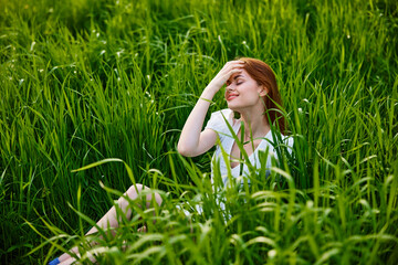 cute woman with red hair sits in tall green grass with her hand on her head