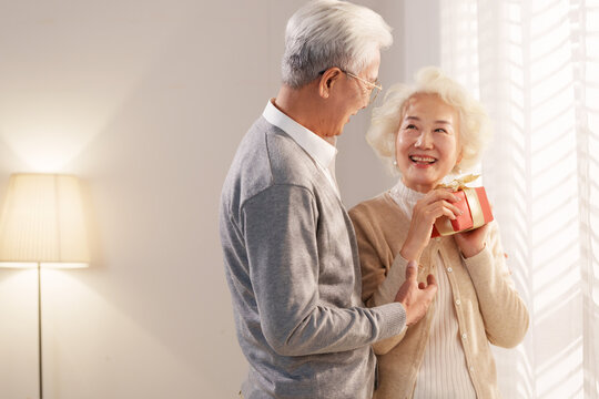 Happy elderly man in front of the window receives a gift from his wife