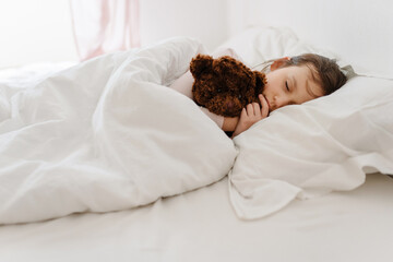 School child sleeps in bed. white alarm clock on foreground of bed and sleeping kid in interior of...