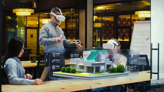 Male designer uses VR headset and wireless controllers, presents smart home exterior design project in virtual reality to coworkers. Modern hi-tech company. 3D hologram. Future digital technologies.
