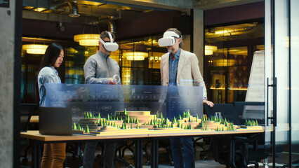 Male architect uses VR headset and wireless controllers, presents modern hi-tech building and park architectural project in virtual reality to colleagues. 3D hologram. Future digital AI technologies. © Framestock