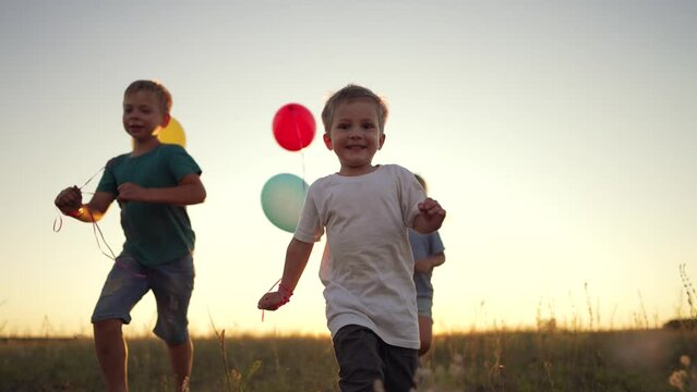 Happy children with balloons. Family run together on the green grass in nature. Children with a smile on their faces play together in the park. Family running in the park at sunset with balloons